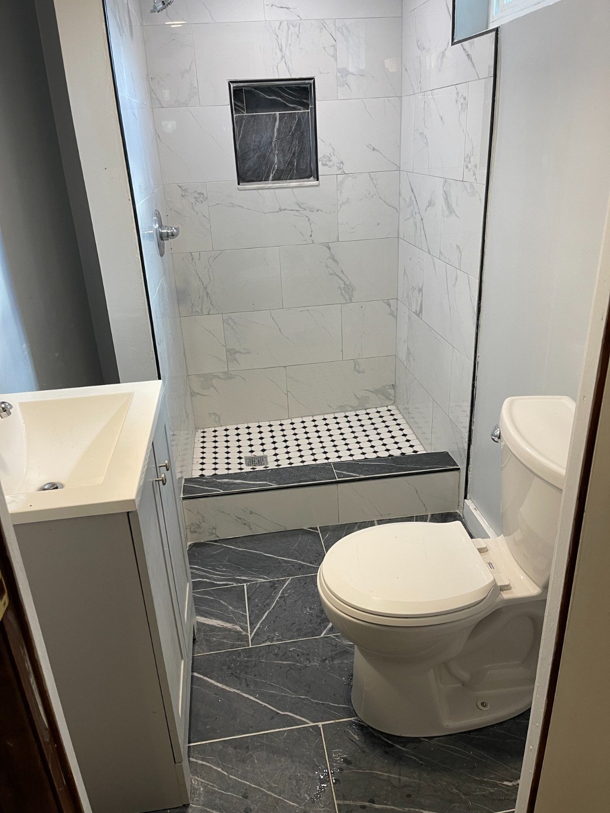Compact bathroom with marble wall tile, mosaic shower pan, and slate floor