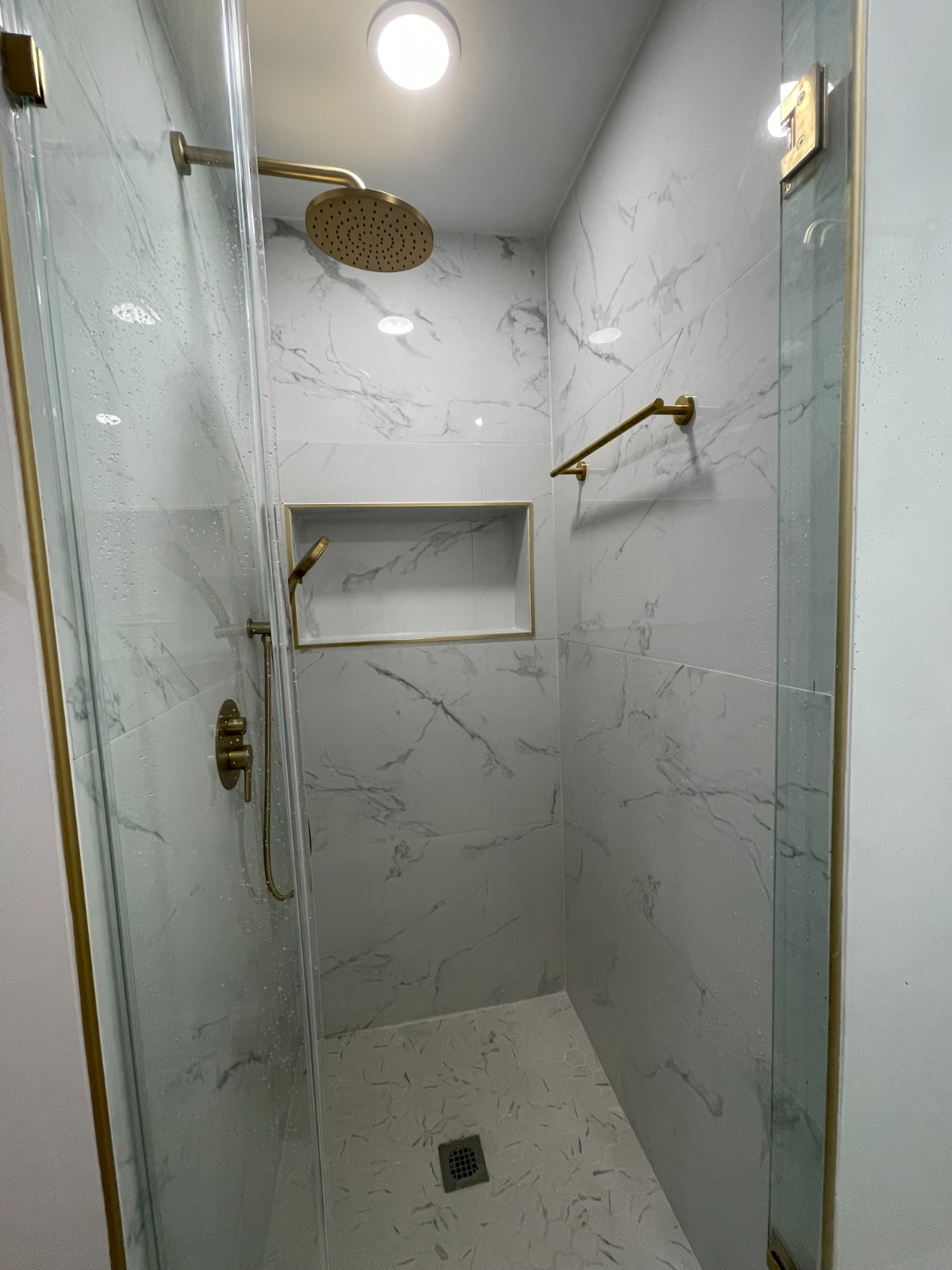 Walk-in shower with marble-look tile and brushed gold fixtures